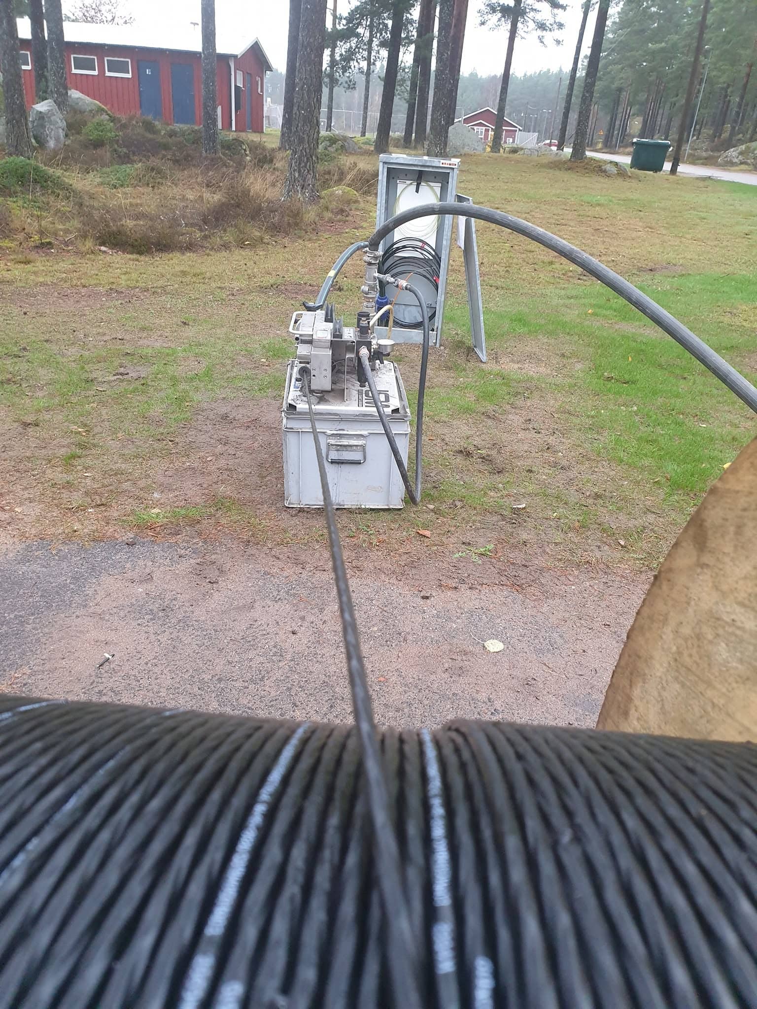 Svart kabeltrumma och blåsmaskin för fiberförläggning vid röda träbyggnader