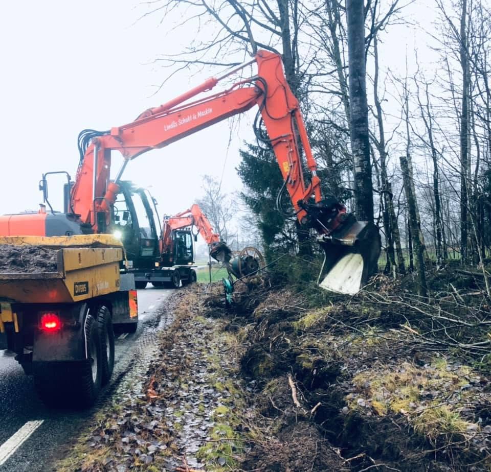 Hitachi med Lindås Schakt & Maskin på bommen, schaktar i vägdike vid kabelhaspel