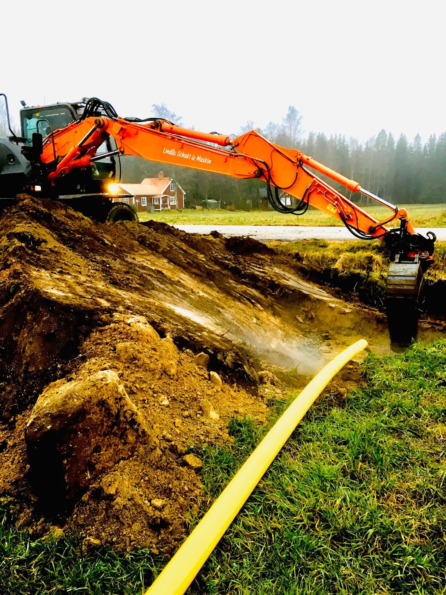 Hitachi med Lindås Schakt & Maskin på bommen, schaktar vid gult skyddsrör
