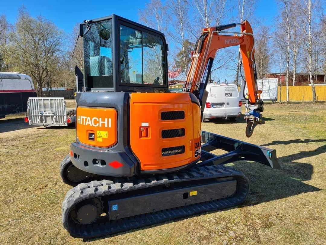 Orange Hitachi-minigrävare på band, med LSM-skyltbil i bakgrunden