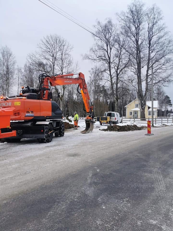 Hitachi ZX140W i vinterarbete vid en landsväg, med personal i varselkläder