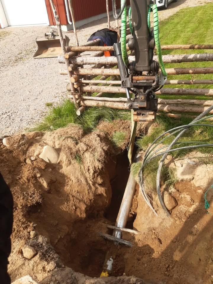 Jordraket med gröna slangar som trycks i ett schakt vid en gärdesgård