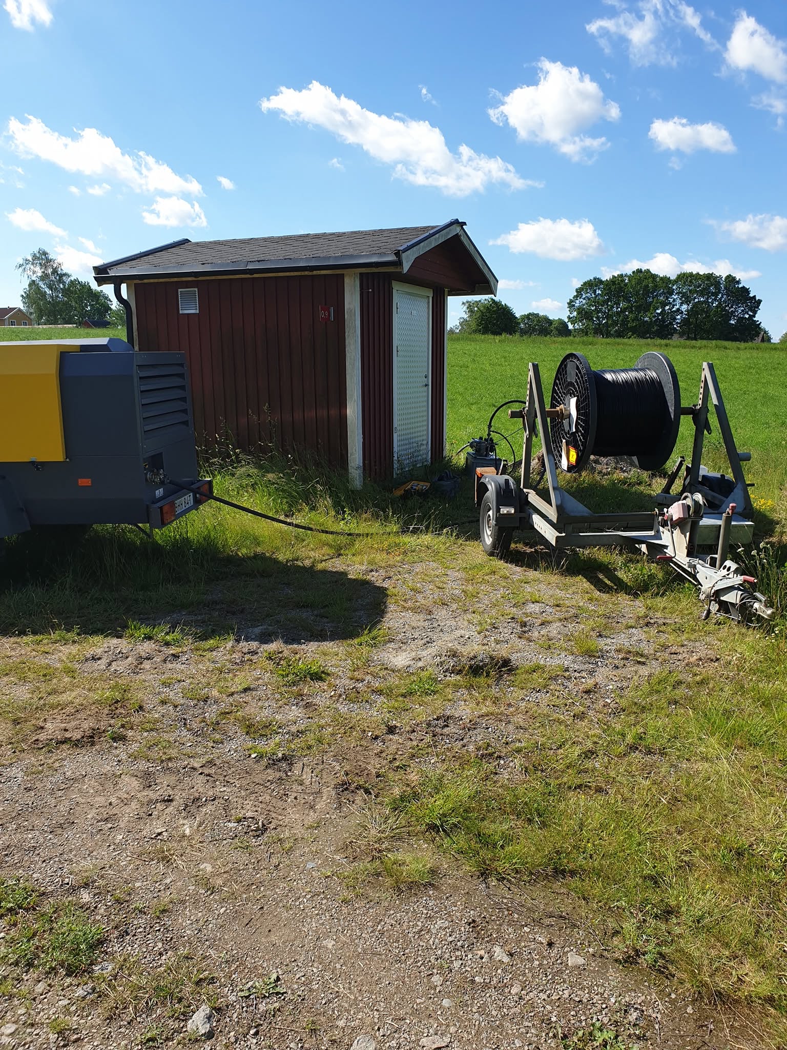 Kabelhaspel och kompressor vid en röd bod under fiberblåsning