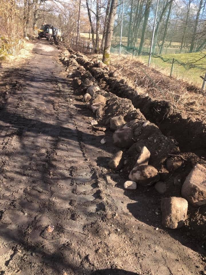 Schaktad väg med sten längs kanten och en maskin längre fram bland träden
