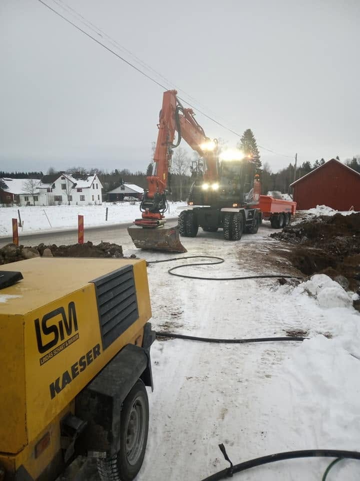 Gul Kaeser-kompressor med LSM-dekal och hjulgrävare i arbete på snöig väg