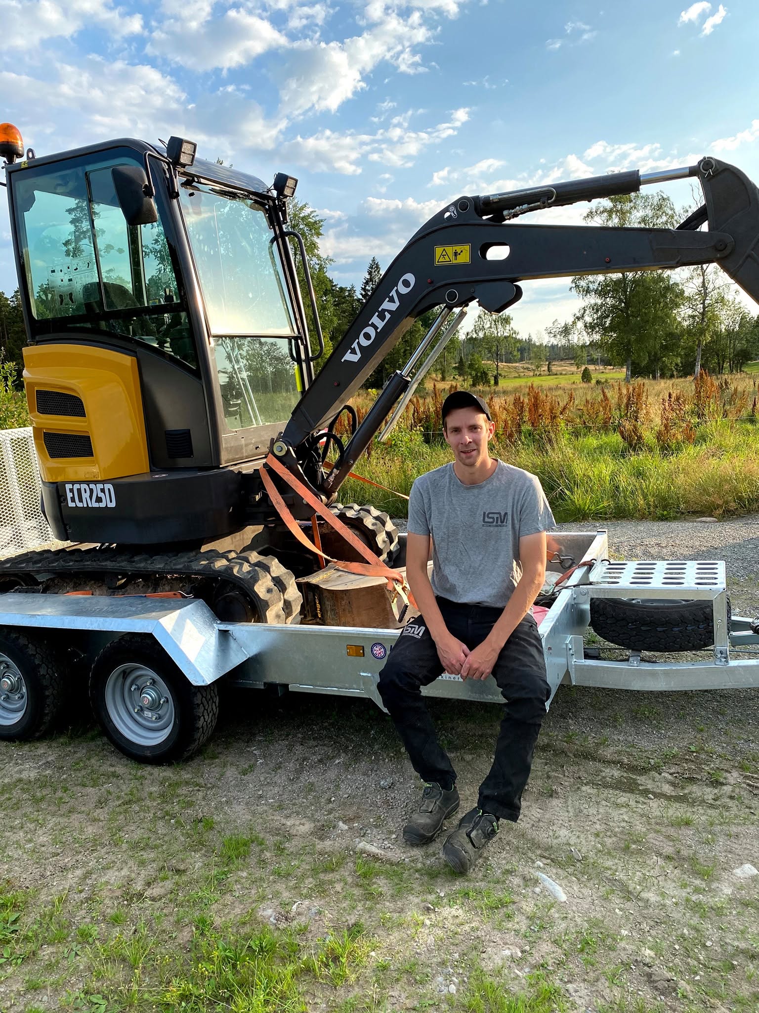 Medarbetare i LSM-tröja sittande på en trailer bredvid en Volvo ECR25D